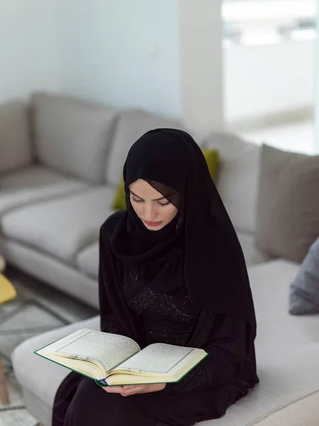 Young traditional Muslim women read Quran on the sofa before iftar dinner during a Ramadan feast at home.