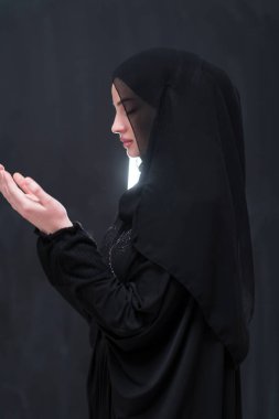 Şık giyinmiş, tesettürlü, güzel Müslüman bir kadının portresi Tanrı 'ya geleneksel dualar yapıyor ve siyah arka planda izole edilmiş dua hareketleriyle el ele tutuşuyor. Yüksek kalite fotoğraf
