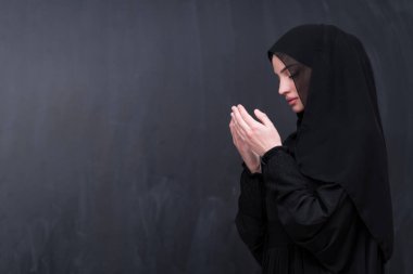 Şık giyinmiş, tesettürlü, güzel Müslüman bir kadının portresi Tanrı 'ya geleneksel dualar yapıyor ve siyah arka planda izole edilmiş dua hareketleriyle el ele tutuşuyor. Yüksek kalite fotoğraf