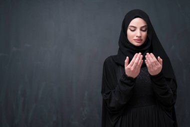 Şık giyinmiş, tesettürlü, güzel Müslüman bir kadının portresi Tanrı 'ya geleneksel dualar yapıyor ve siyah arka planda izole edilmiş dua hareketleriyle el ele tutuşuyor. Yüksek kalite fotoğraf