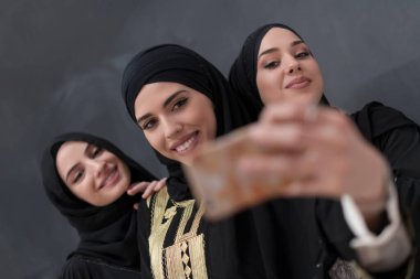Siyah arkaplan önünde fotoğraf çekilirken akıllı telefon kullanan şık giyinmiş bir grup güzel Müslüman kadın. Yüksek kalite fotoğraf