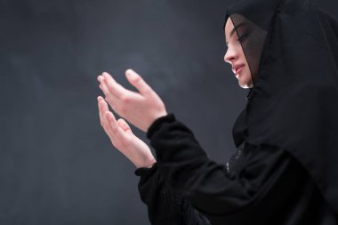 Şık giyinmiş, tesettürlü, güzel Müslüman bir kadının portresi Tanrı 'ya geleneksel dualar yapıyor ve siyah arka planda izole edilmiş dua hareketleriyle el ele tutuşuyor. Yüksek kalite fotoğraf