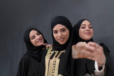 Siyah arkaplan önünde fotoğraf çekilirken akıllı telefon kullanan şık giyinmiş bir grup güzel Müslüman kadın. Yüksek kalite fotoğraf