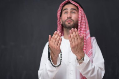 Geleneksel kıyafetlerle Tanrı 'ya dua eden genç bir Arap adam ellerini siyah bir arkaplan önünde dua ederek tutar. Yüksek kalite fotoğraf
