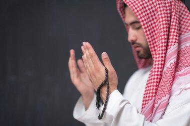 Geleneksel kıyafetlerle Tanrı 'ya dua eden genç bir Arap adam ellerini siyah bir arkaplan önünde dua ederek tutar. Yüksek kalite fotoğraf