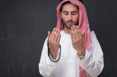 Geleneksel kıyafetlerle Tanrı 'ya dua eden genç bir Arap adam ellerini siyah bir arkaplan önünde dua ederek tutar. Yüksek kalite fotoğraf