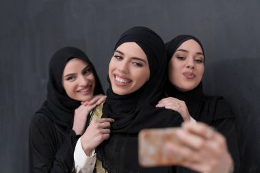 Siyah arkaplan önünde fotoğraf çekilirken akıllı telefon kullanan şık giyinmiş bir grup güzel Müslüman kadın. Yüksek kalite fotoğraf