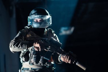 Saldırı tüfeği ve miğfer takan savaş üniformalı asker karanlık bir geçmişi var. Mavi ve mor jel ışık efekti. Yüksek kalite fotoğraf