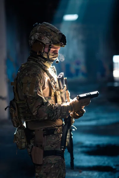 Soldier of army elite forces, special security service fighter with hidden behind mask and glasses face, in helmet and load carriage system, aiming with service pistol low key. High quality photo