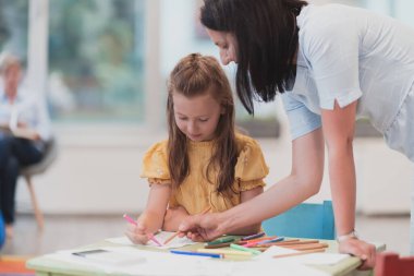 Bir kreşteki sanat dersinde yaratıcı çocuklar ya da ilkokul sınıfında bayan bir öğretmenle resim çizen çocuklar.. 