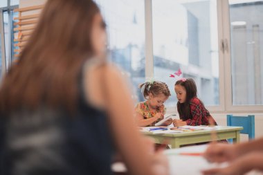 Bir kreşteki sanat dersinde yaratıcı çocuklar ya da ilkokul sınıfında bayan bir öğretmenle resim çizen çocuklar.. 