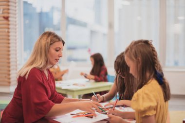 Bir kreşteki sanat dersinde yaratıcı çocuklar ya da ilkokul sınıfında bayan bir öğretmenle resim çizen çocuklar.. 