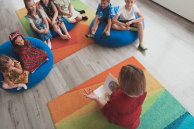 İlkokulda ya da anaokulunda okuyan bir öğretmen, bir ilkokulda ya da anaokulunda çocuklara kitap okur. Okul öncesi eğitim kavramı. Seçici odak. 