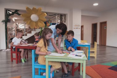 Bir kreşteki sanat dersinde yaratıcı çocuklar ya da ilkokul sınıfında bayan bir öğretmenle resim çizen çocuklar.. 