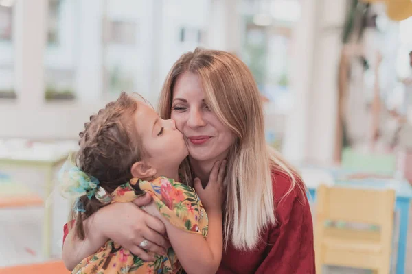 一个可爱的小女孩在幼儿园里亲吻和拥抱她的母亲 — 图库照片