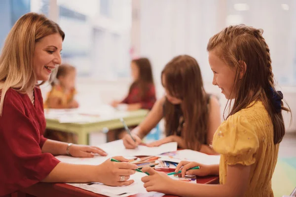 Bir kreşteki sanat dersinde yaratıcı çocuklar ya da ilkokul sınıfında bayan bir öğretmenle resim çizen çocuklar.. 