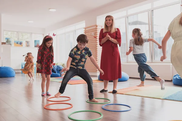 Small nursery school children with a female teacher on the floor indoors in the classroom, doing exercise. Jumping over hula hoop circles track on the floor. High quality photo