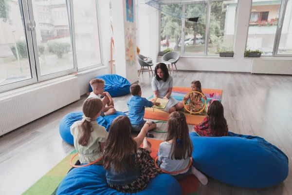 Reading time in an elementary school or kindergarten, a teacher reads a book to children in an elementary school or kindergarten. The concept of pre-school education. Selective focus.