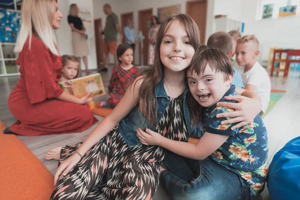 A girl and a boy with Downs syndrome in each others arms spend time together in a preschool institution. High quality photo