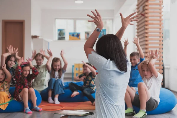 一位快乐的女教师与一群小学生坐在一起玩手游 免版税图库图片