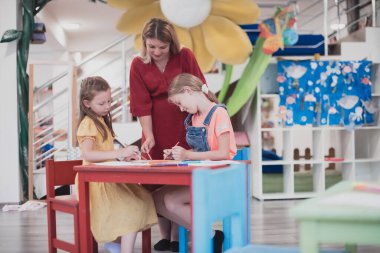 Bir kreşteki sanat dersinde yaratıcı çocuklar ya da ilkokul sınıfında bayan bir öğretmenle resim çizen çocuklar.. 