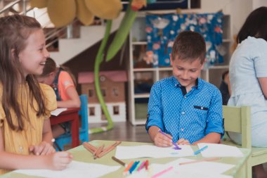 Sevimli kız ve oğlan anaokulunda birlikte oturup resim çiziyorlar. Yüksek kaliteli fotoğraf.
