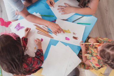 Bir kreşteki sanat dersinde yaratıcı çocuklar ya da ilkokul sınıfında bayan bir öğretmenle resim çizen çocuklar.. 