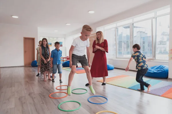 Small nursery school children with a female teacher on the floor indoors in the classroom, doing exercise. Jumping over hula hoop circles track on the floor. High quality photo