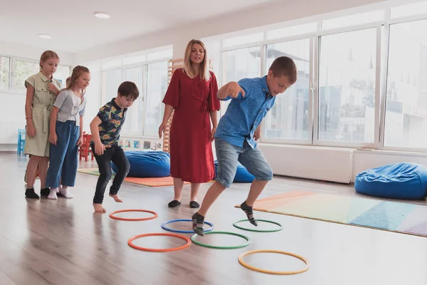 Small nursery school children with a female teacher on the floor indoors in the classroom, doing exercise. Jumping over hula hoop circles track on the floor. High quality photo