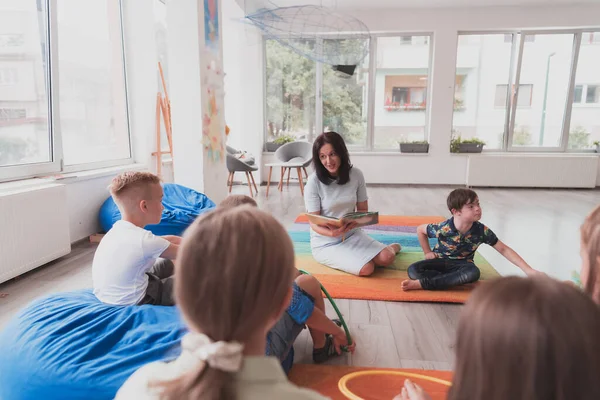 Reading time in an elementary school or kindergarten, a teacher reads a book to children in an elementary school or kindergarten. The concept of pre-school education. Selective focus.