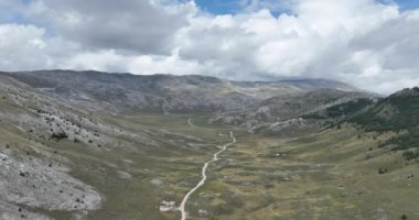 Yeşil tarlalar arasındaki platoda boş asfalt yol, hava manzaralı. Dağlar arasında terk edilmiş tarlaları geçmek için uzun ve açık bir yol üzerinden uçmak. Manzaralı Highland yolu. Konsept araba yolculuğu. Çöl