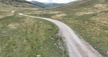 Yeşil tarlalar arasındaki platoda boş asfalt yol, hava manzaralı. Dağlar arasında terk edilmiş tarlaları geçmek için uzun ve açık bir yol üzerinden uçmak. Manzaralı Highland yolu. Konsept araba yolculuğu. Çöl