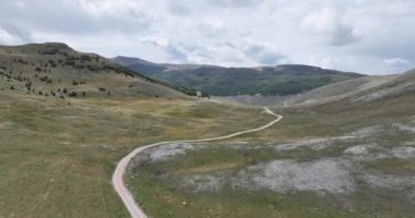 Yeşil tarlalar arasındaki platoda boş asfalt yol, hava manzaralı. Dağlar arasında terk edilmiş tarlaları geçmek için uzun ve açık bir yol üzerinden uçmak. Manzaralı Highland yolu. Konsept araba yolculuğu. Çöl