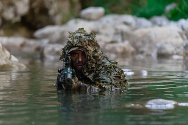 Askeri bir adam ya da kamuflaj kıyafetli bir havalı oyuncu nehri gizlice geçerek bir keskin nişancı tüfeğinden ya da hedefe nişan alır. Yüksek kalite fotoğraf