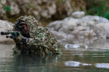 Askeri bir adam ya da kamuflaj kıyafetli bir havalı oyuncu nehri gizlice geçerek bir keskin nişancı tüfeğinden ya da hedefe nişan alır. Yüksek kalite fotoğraf