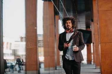 Finans bölgesinde deri çantalı modaya uygun bir iş adamı. Akıllı telefon kullanıyor. Ses şarkıları dinliyor, kahve içiyor. Yüksek kalite fotoğraf