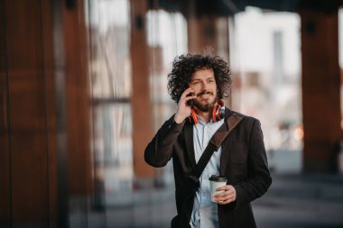 Finans bölgesinde deri çantalı modaya uygun bir iş adamı. Akıllı telefon kullanıyor. Ses şarkıları dinliyor, kahve içiyor. Yüksek kalite fotoğraf