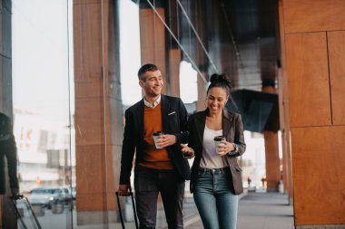 İş adamı ve iş kadını konuşuyor ve bavullarını tutuyor iş seyahatinde, ellerinde taze kahve taşıyorlar. İş konsepti. Yüksek kalite fotoğraf