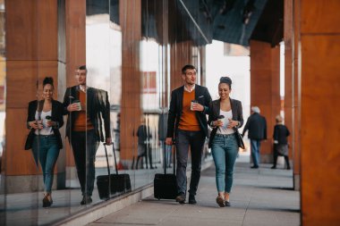 İş adamı ve iş kadını konuşuyor ve bavullarını tutuyor iş seyahatinde, ellerinde taze kahve taşıyorlar. İş konsepti. Yüksek kalite fotoğraf