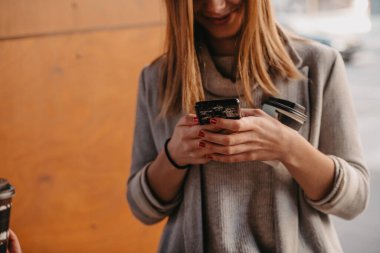 Bir kızın kahve içerken ve işten çıkarken cep telefonu kullanırken çekilmiş makro fotoğrafı. Yüksek kalite fotoğraf