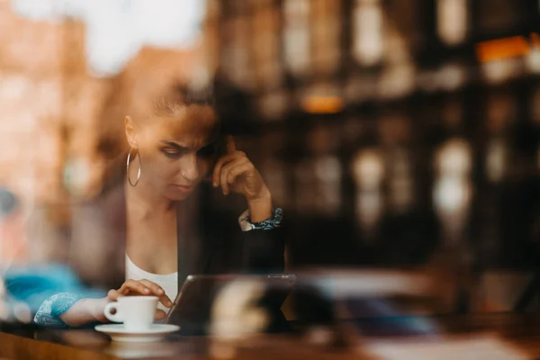 woman in a coffee shop drink coffee viewed through glass with reflections as they sit at a table chatting and laughing. High quality photo