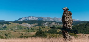 Ordu askeri dürbünlü bir keskin nişancı tüfeği tutuyor ve ormanda yürüyor. Savaş, ordu, teknoloji ve insan kavramı. Yüksek kalite fotoğraf