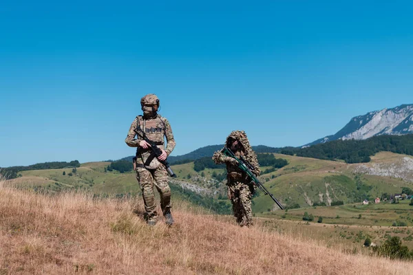A sniper team squad of soldiers is going undercover. Sniper assistant and team leader walking and aiming in nature with yellow grass and blue sky. Tactical camouflage uniform. Hi quality stock photo.