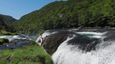 FPV Aerial doğal manzara nehri Una 'da Strbacki Buk şelalesiyle ağaçların altındaki yoğun yeşil ormanda uçma becerisini yakaladı. Yüksek kalite 4k görüntü