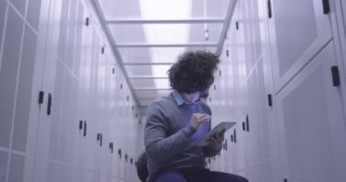 Modern bir sanal veri merkezi süperbilgisayarının sunucu odasında tablet bilgisayar üzerinde çalışan bilişim mühendisi ya da veri bilimci. Hippi gündelik kıyafetler giyer ve bir sandalyeye oturur.. 