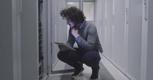 在现代云计算虚拟数据中心超级计算机的服务器室内从事平板计算机工作的It工程师或数据科学专家 穿着休闲装在机架走廊工作的嬉皮士 — 图库视频影像