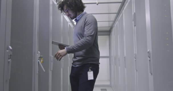 在现代云计算虚拟数据中心超级计算机的服务器室内从事平板计算机工作的It工程师或数据科学专家 穿着休闲装在机架走廊工作的嬉皮士 — 图库视频影像