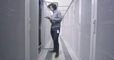 Modern bir sanal veri merkezi süperbilgisayarının sunucu odasında tablet bilgisayar üzerinde çalışan bilişim mühendisi ya da veri bilimci. Günlük kıyafetler giyen hippi, askı koridorunda çalışıyor.
