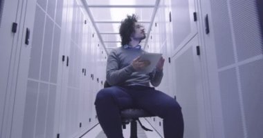 Modern bir sanal veri merkezi süperbilgisayarının sunucu odasında tablet bilgisayar üzerinde çalışan bilişim mühendisi ya da veri bilimci. Hippi gündelik kıyafetler giyer ve bir sandalyeye oturur.. 