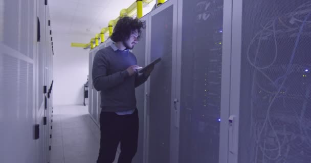 Itエンジニアやデータサイエンスの専門家は 現代のクラウドコンピューティング仮想データセンタースーパーコンピュータのサーバールームでタブレットコンピュータに取り組んでいます ラック廊下を歩くカジュアル服を身に着けているヒップスター — ストック動画
